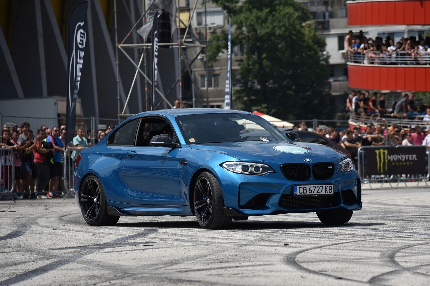 Blue coupe with sporty front and black wheels on event track.