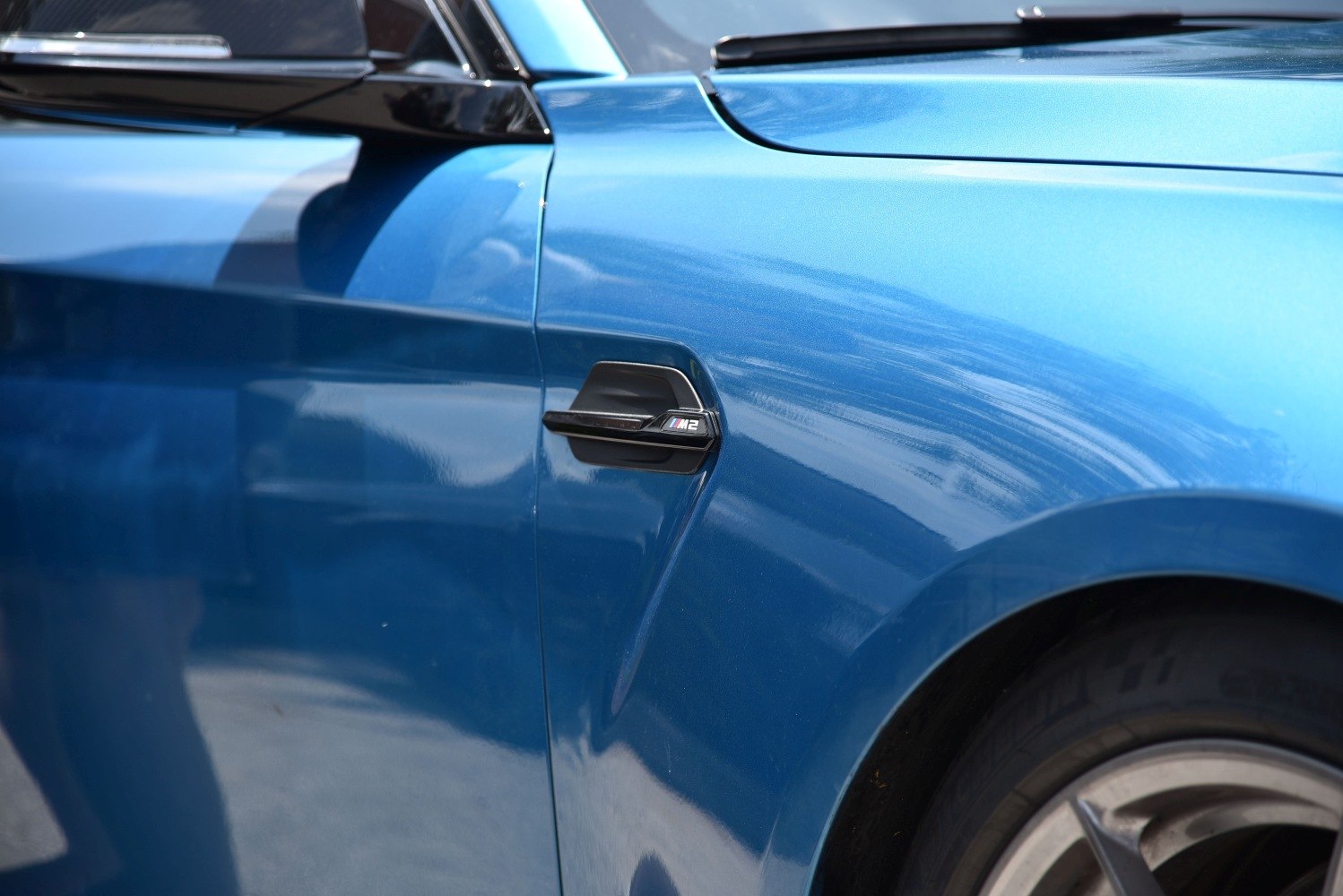 Close-up of car side vent with M2 badge and front wheel rim in blue.