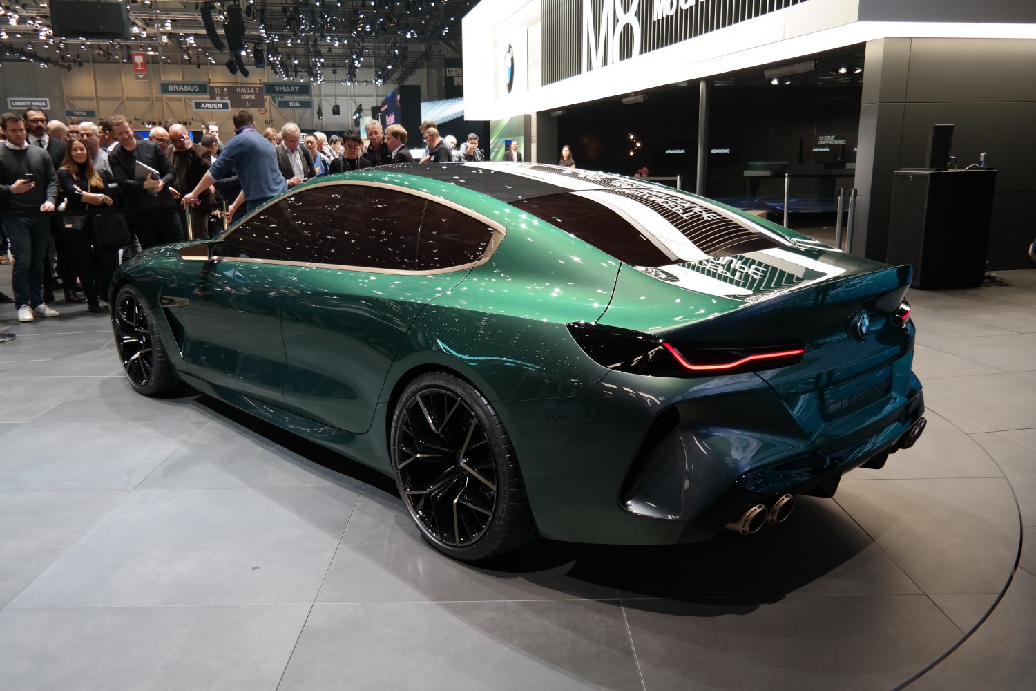 Rear and side view of a sleek green coupe with black alloy wheels, distinct tail lights, and quad exhaust.