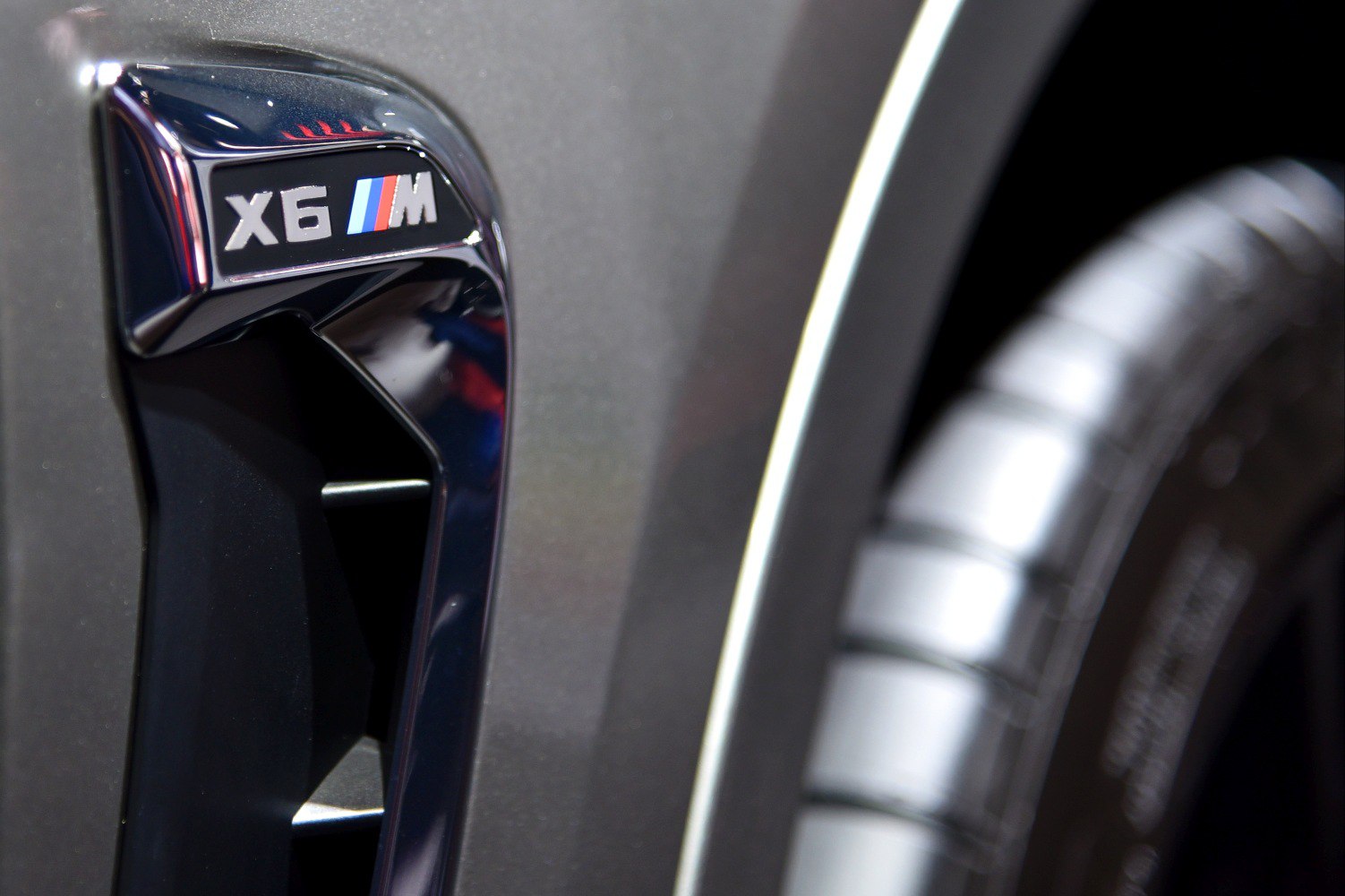 Close-up of side vent with X6 M badge and part of a tire.