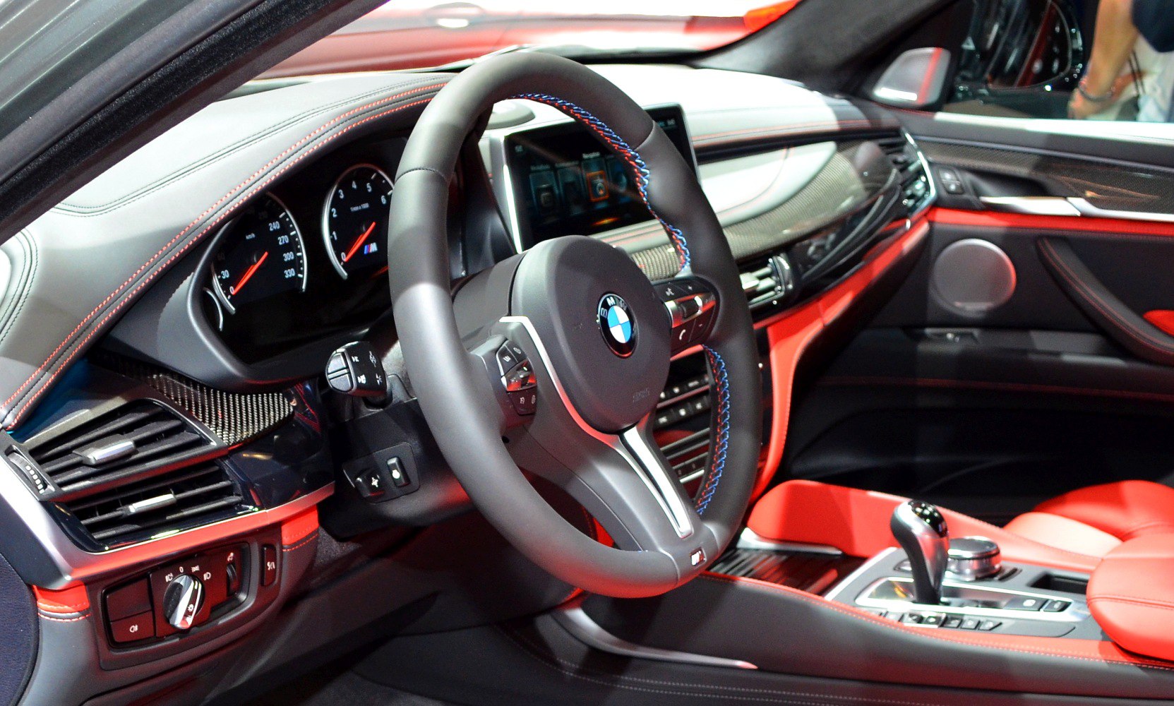 Modern BMW M sport steering wheel with dashboard and red leather interior.