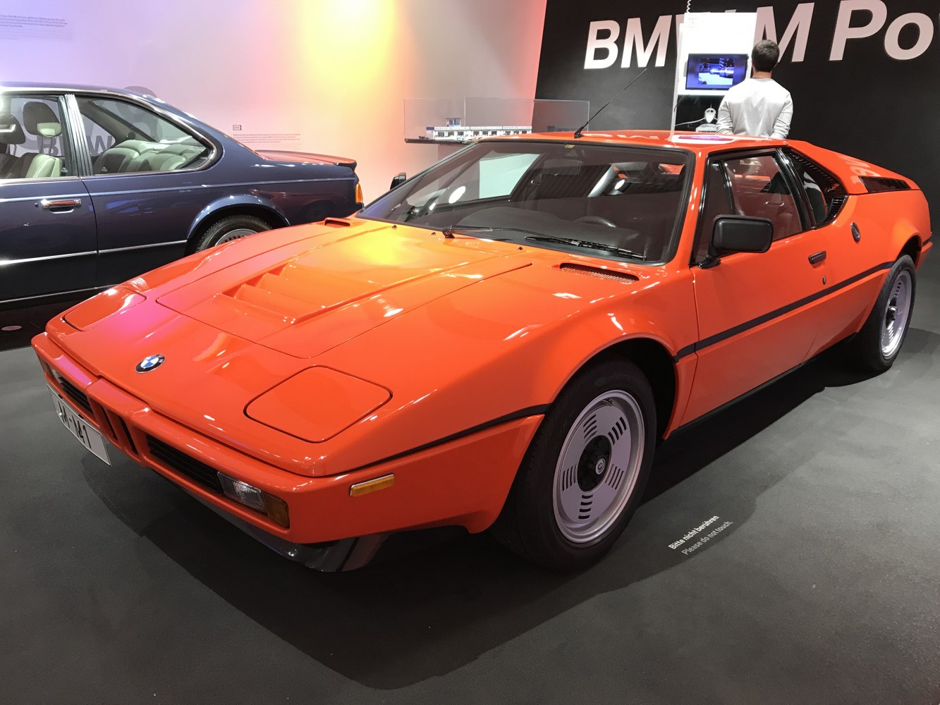 Front side view of an orange vintage sports car with distinctive wheel design.