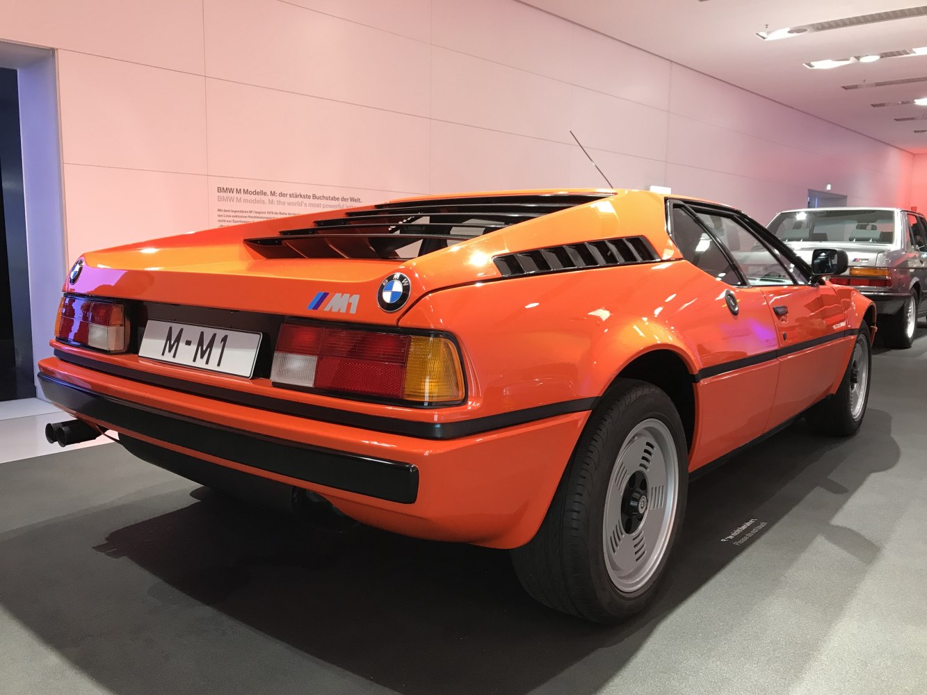 Rear and side view of a bright orange mid-engine sports car with distinct vents and alloy wheels.