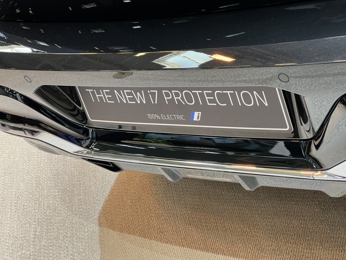 Close-up license plate and rear bumper with 'The New i7 Protection' and 100% Electric text.