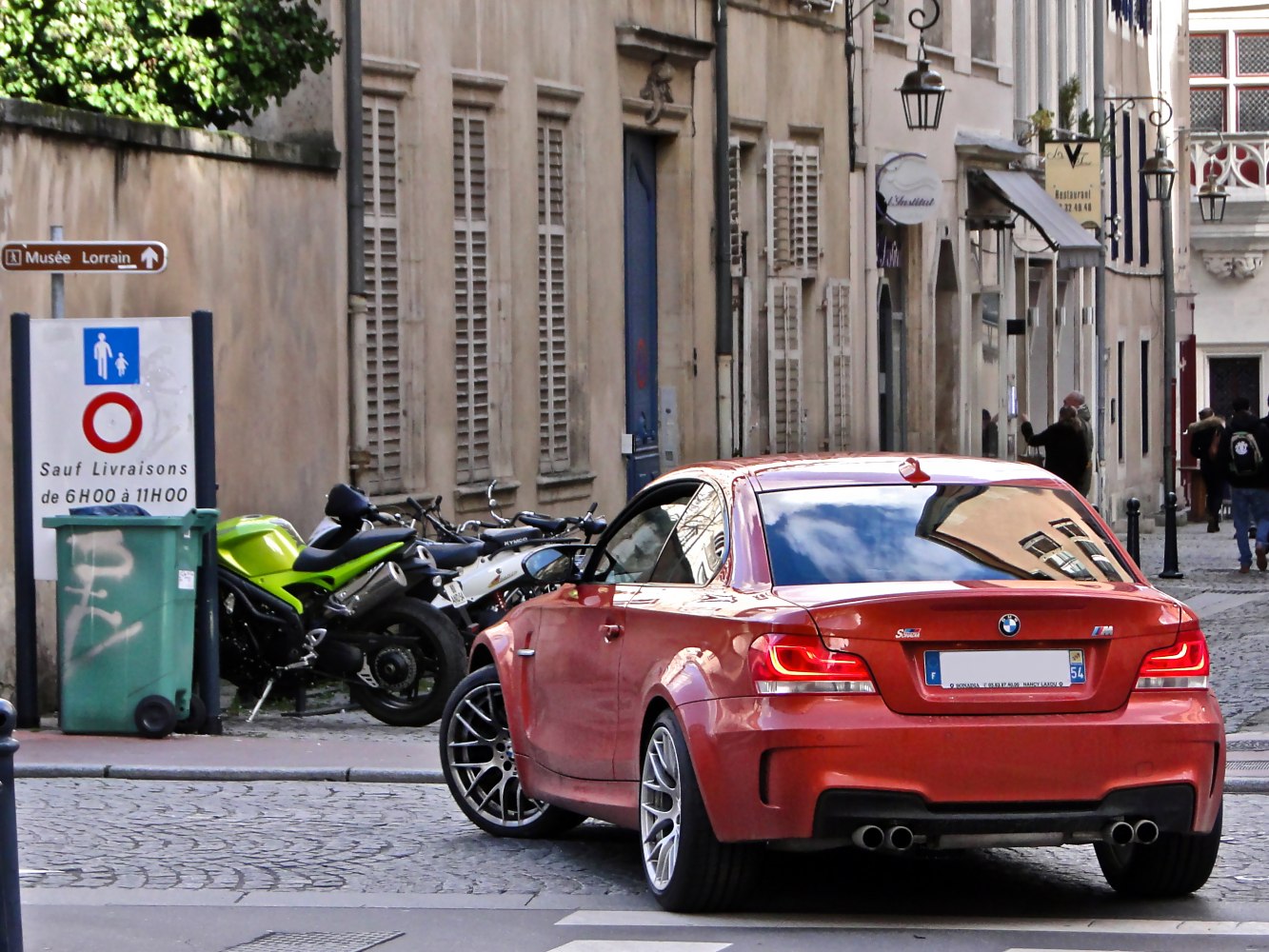 Red sporty coupe with quad exhaust and wide rear wheels in urban street.
