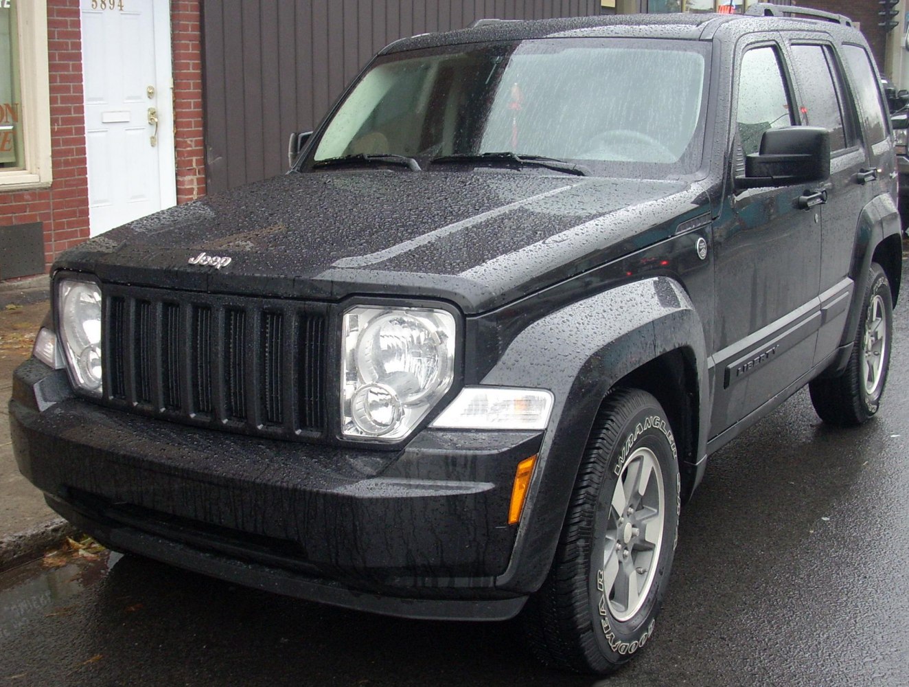Black SUV with vertical grille and square headlights on wet road.