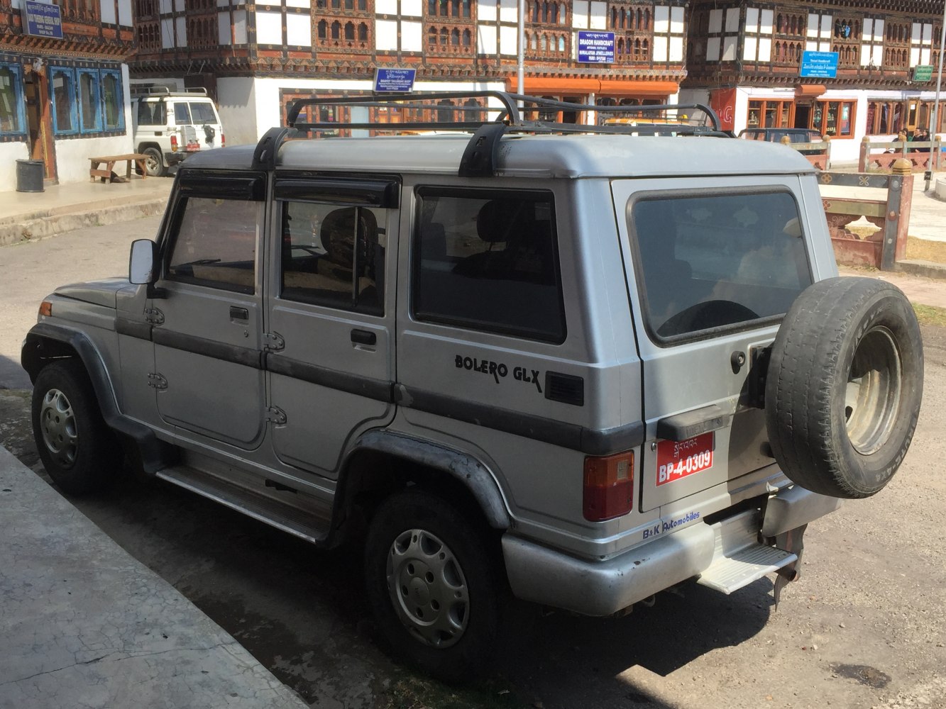 Silver SUV with four doors, roof rack, tinted windows, and rear spare tire