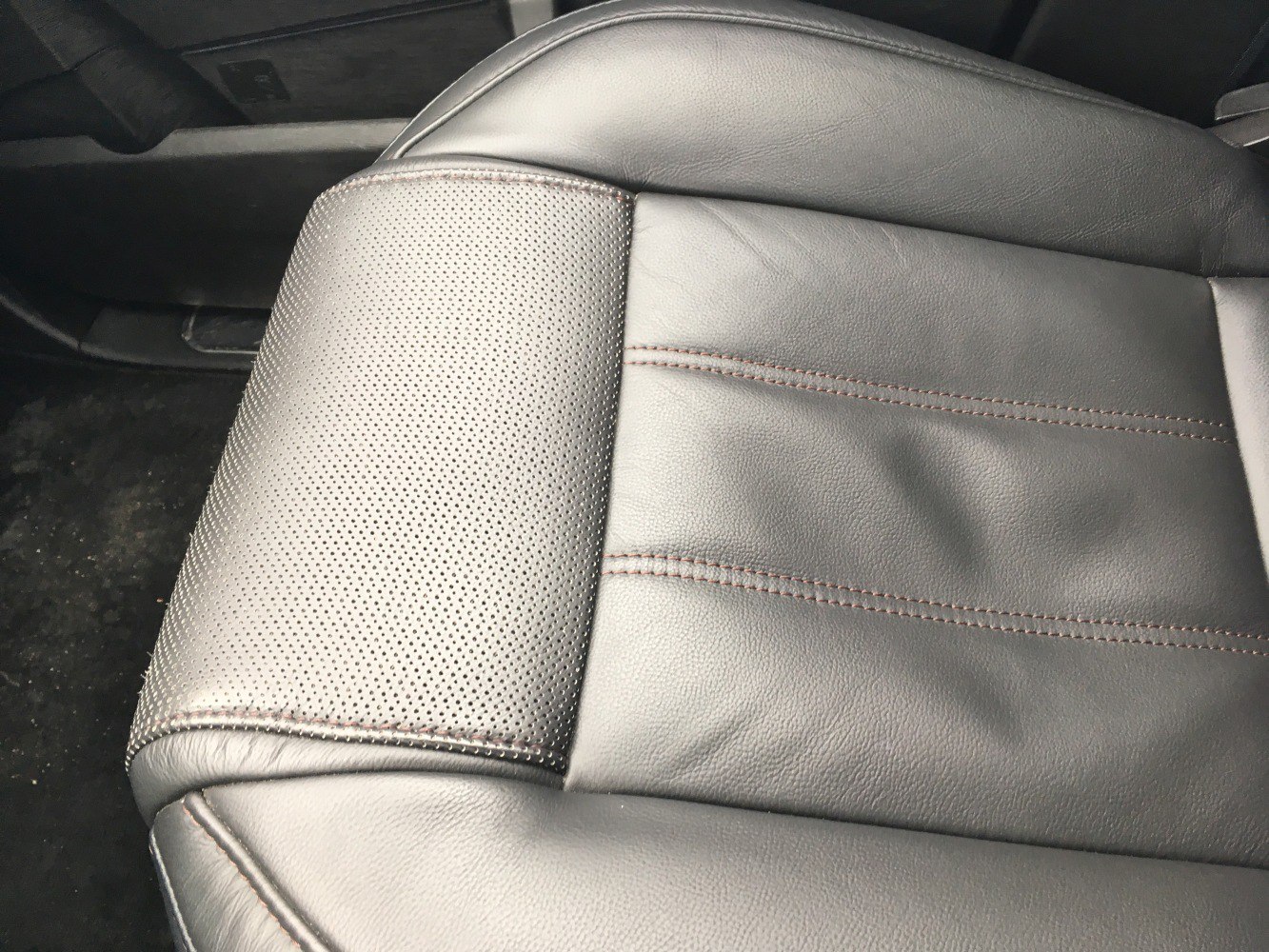 Close-up of perforated and stitched black leather car seat upholstery.
