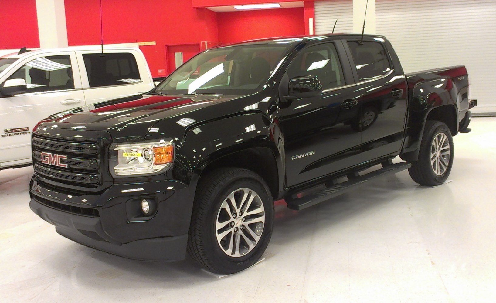 Black crew cab pickup with front grille, fog lights, and alloy wheels in showroom