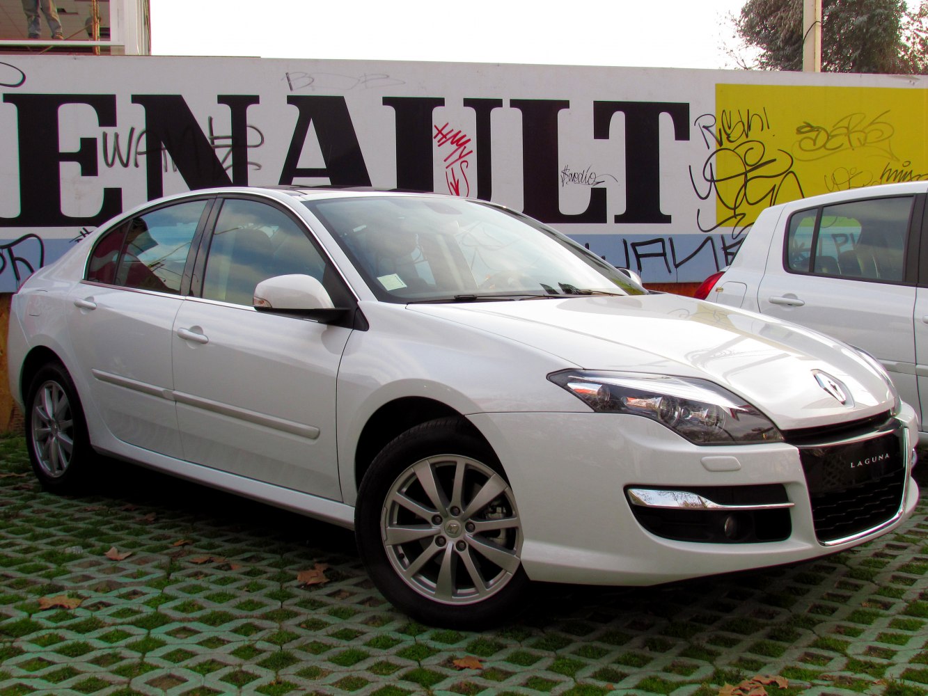 White sedan front side with alloy wheels, parked near graffiti wall