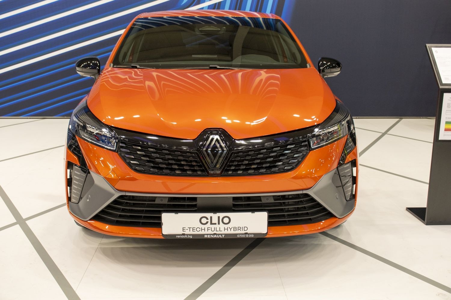 Front view of orange compact car with distinct grille and hybrid badge