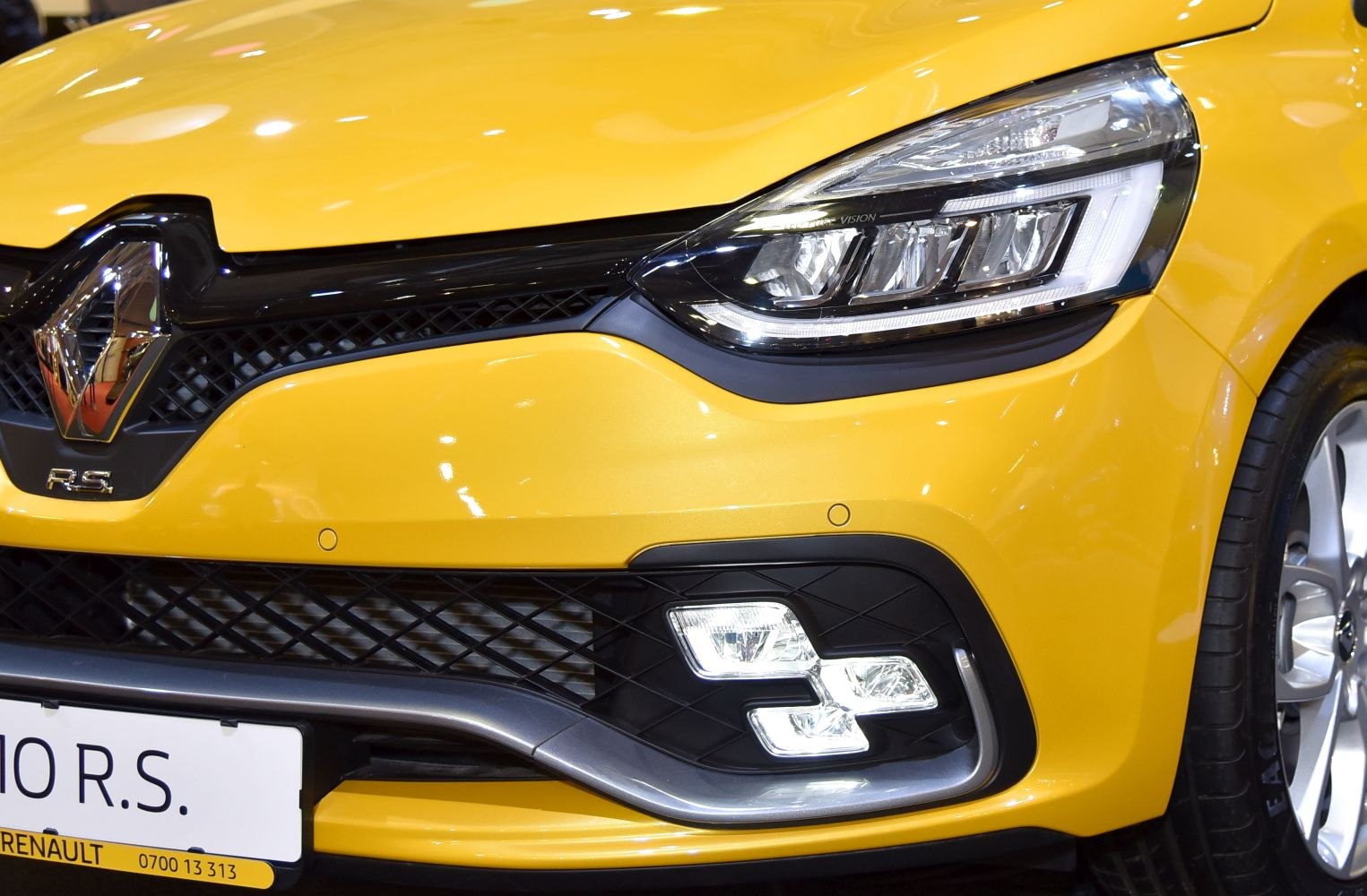 Close-up of headlight, grille, and fog lights on a yellow car front