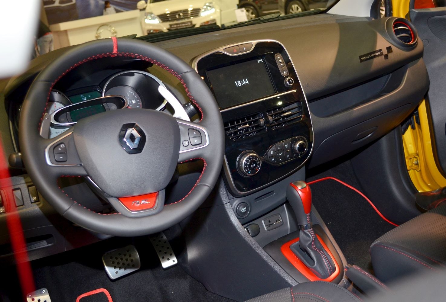 Steering wheel, touchscreen dashboard, gear shifter, and pedals with red accents