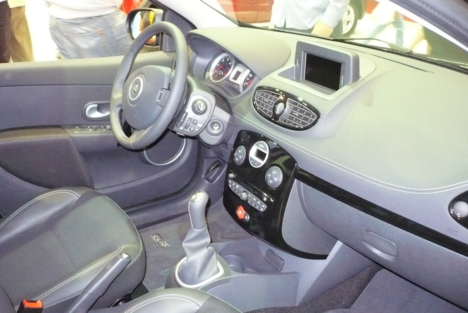 Interior dashboard with steering wheel, infotainment screen, manual gear lever.