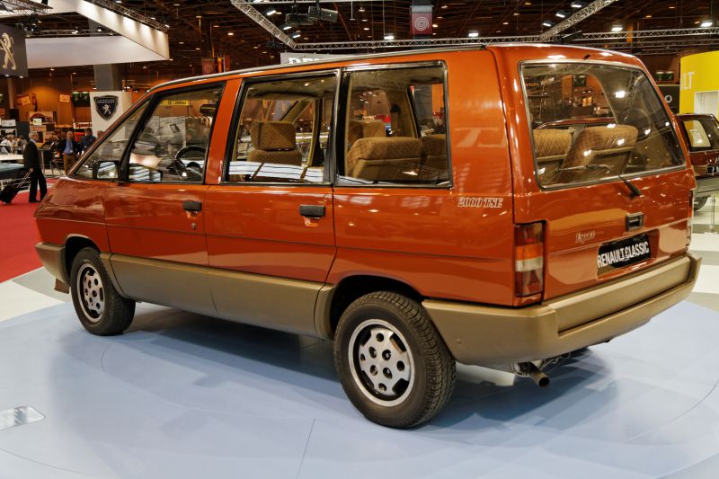 Rear side view of an orange classic minivan with angular design and large windows.