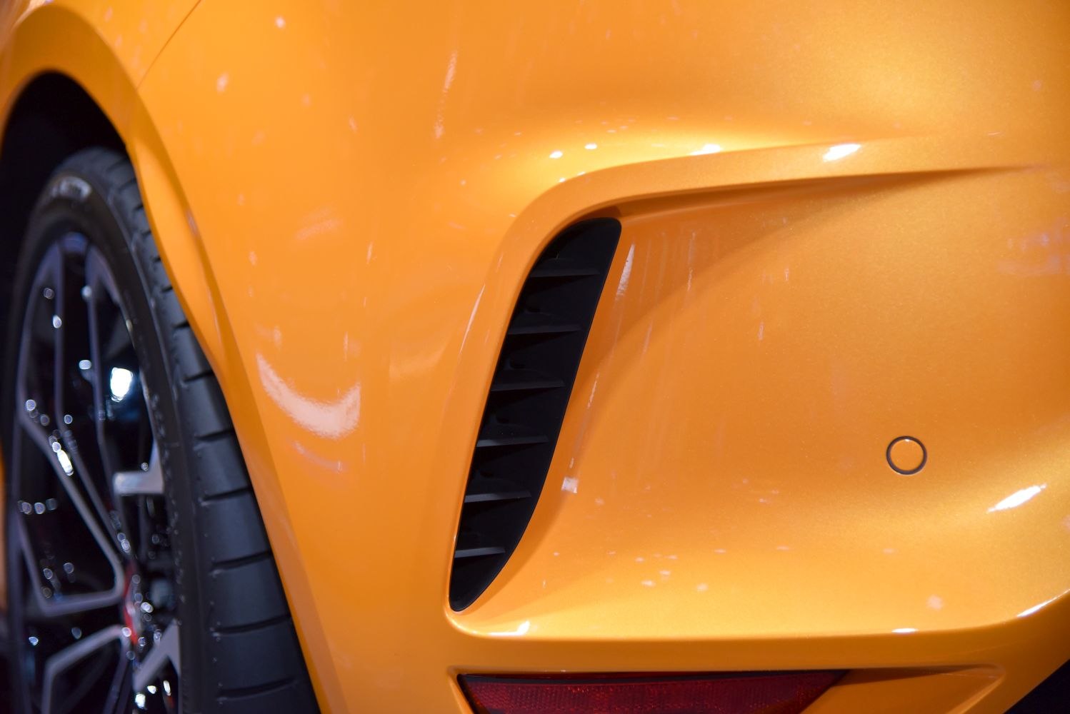Rear air vent with black fins and a black alloy wheel on orange body.