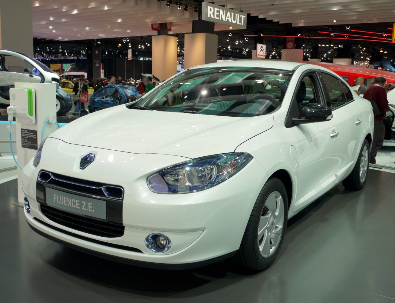 White electric sedan front view with charging station at auto exhibition