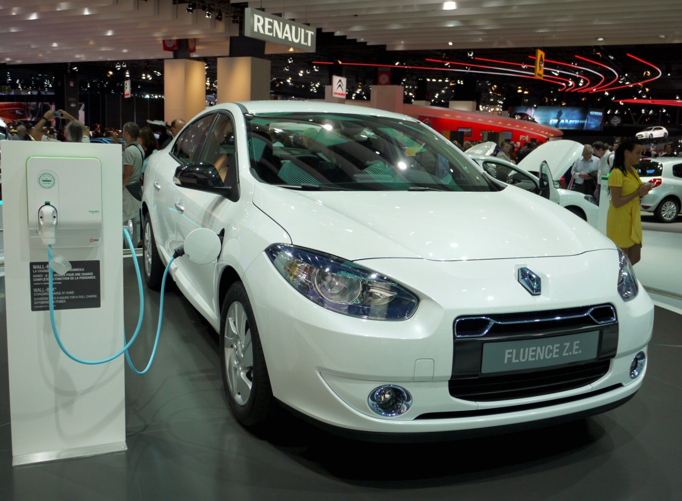 White electric sedan connected to charging station indoors.