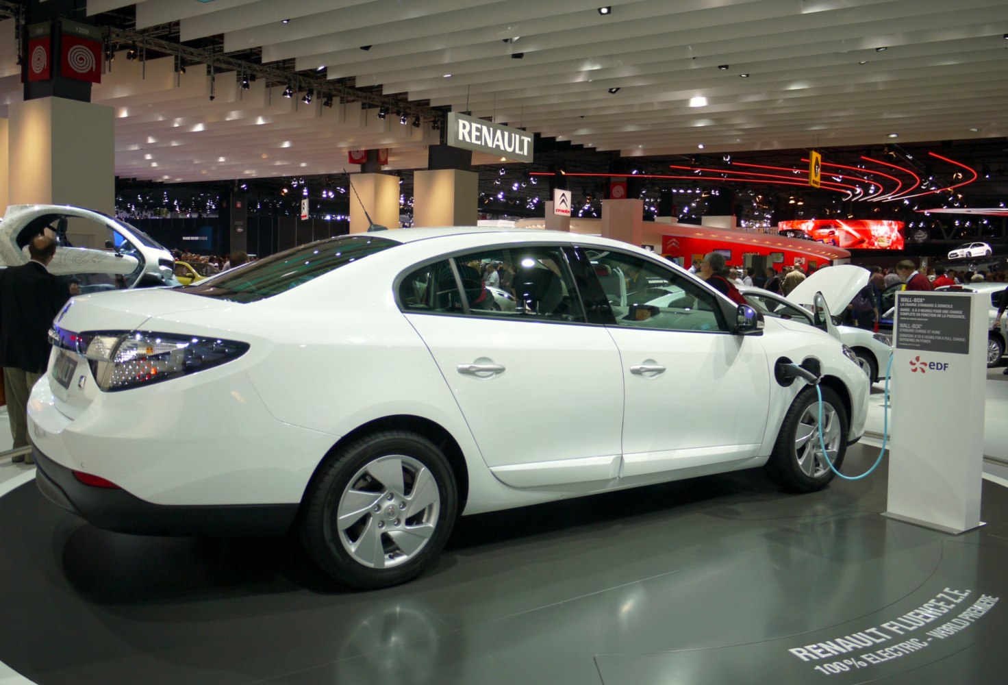 White electric sedan plugged into charging station at auto show