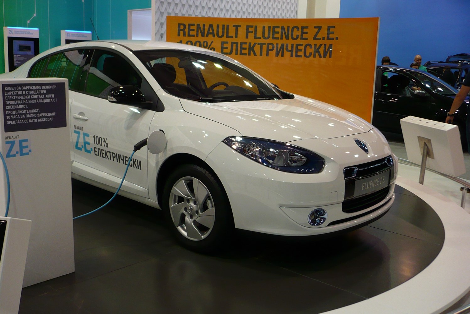 White electric sedan charging at a public exhibition