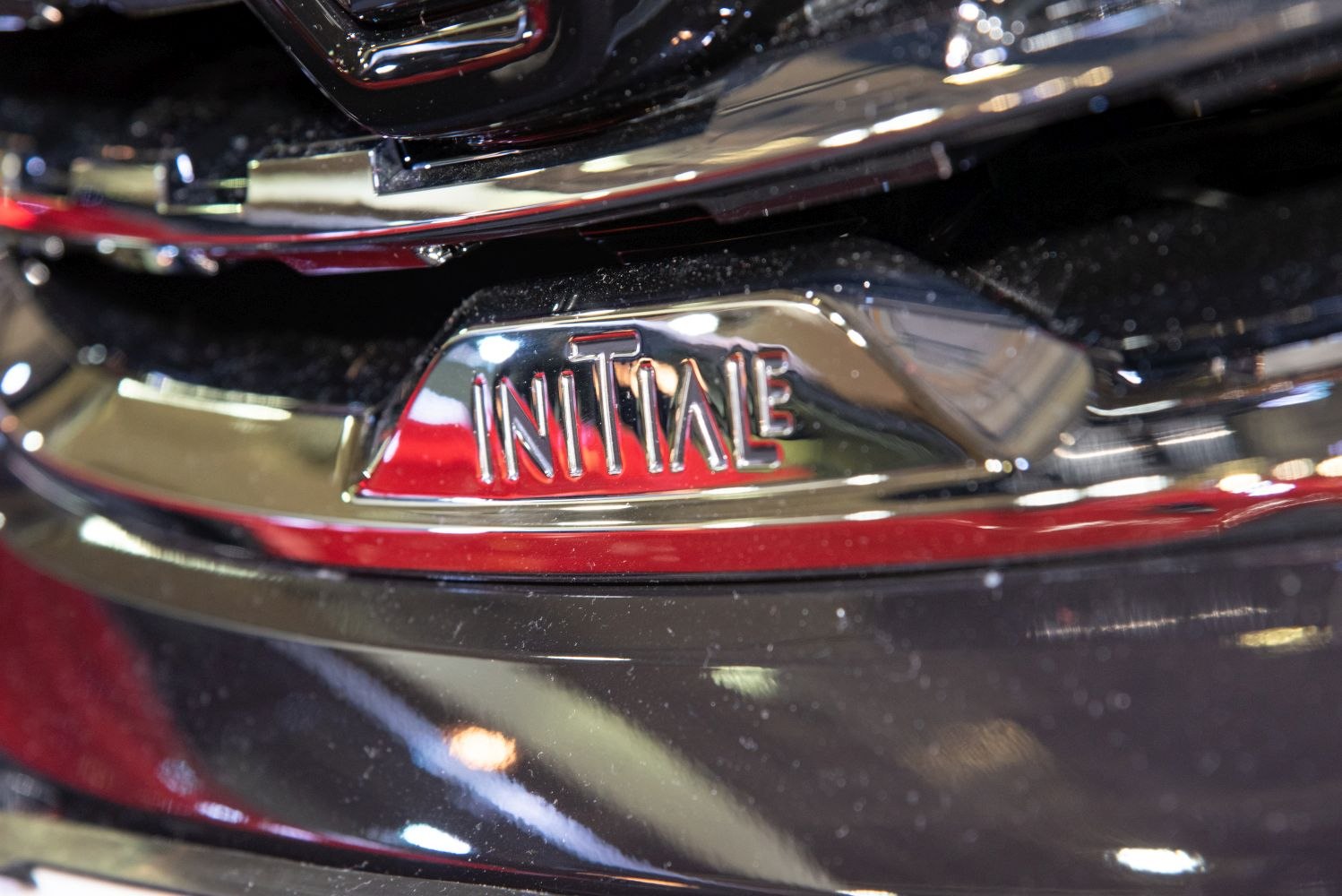 Close-up of a chrome Initiale badge on vehicle front.