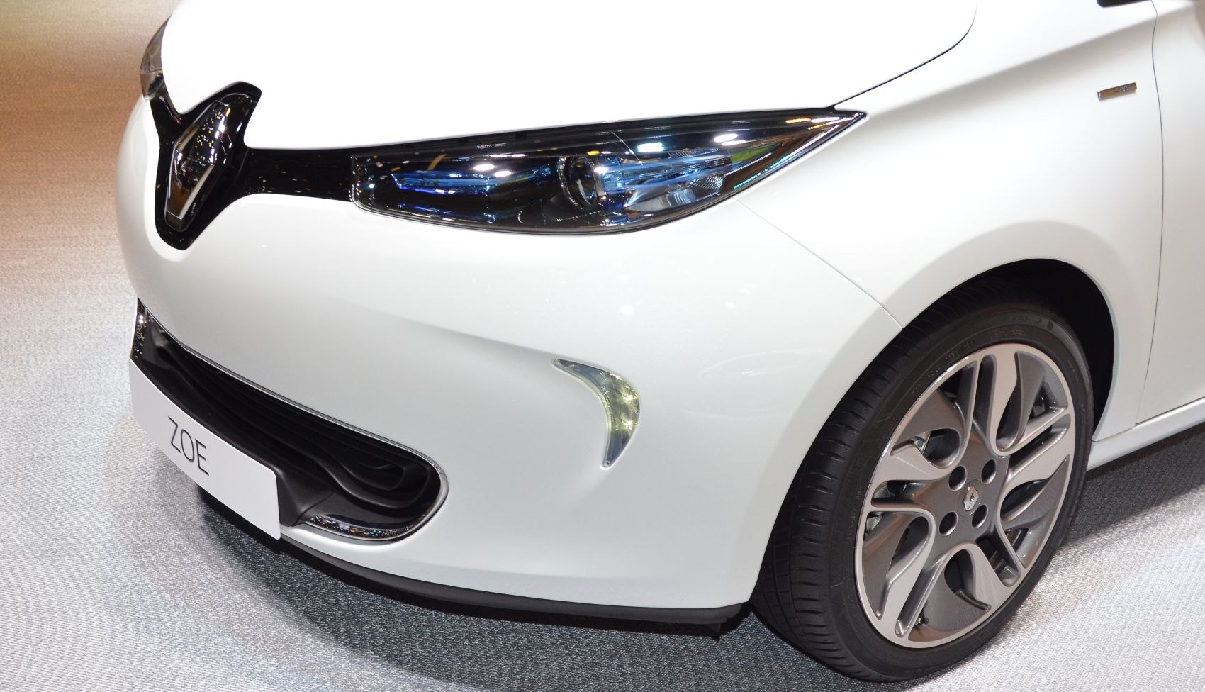 Front close-up of car headlight, grille, and alloy wheel on white body.