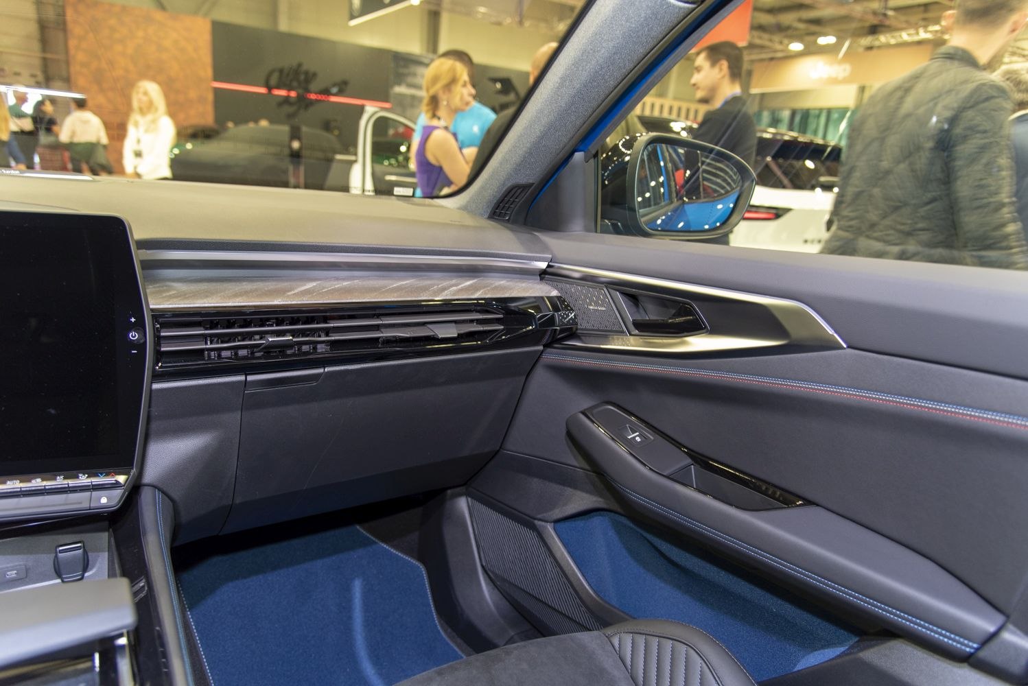 Modern car interior with dashboard and door panel featuring blue stitching.