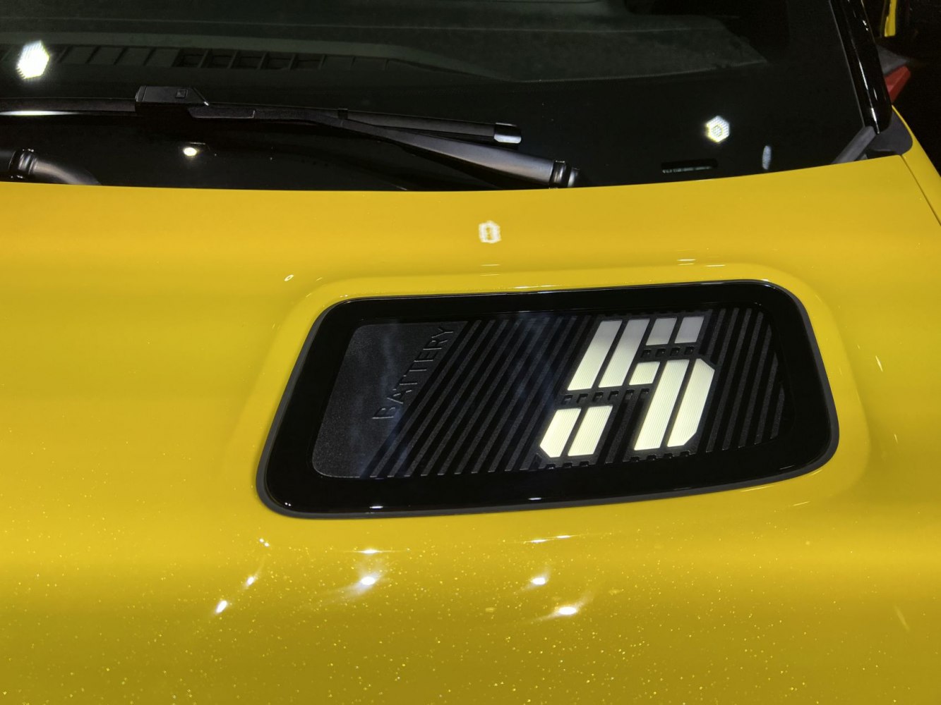 Close-up of Renault 5 E-Tech battery emblem on yellow hood