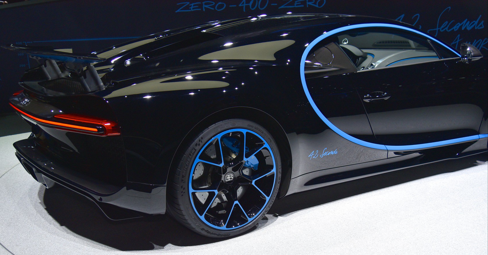 Rear view of sports car with blue-accented wheels and active rear spoiler