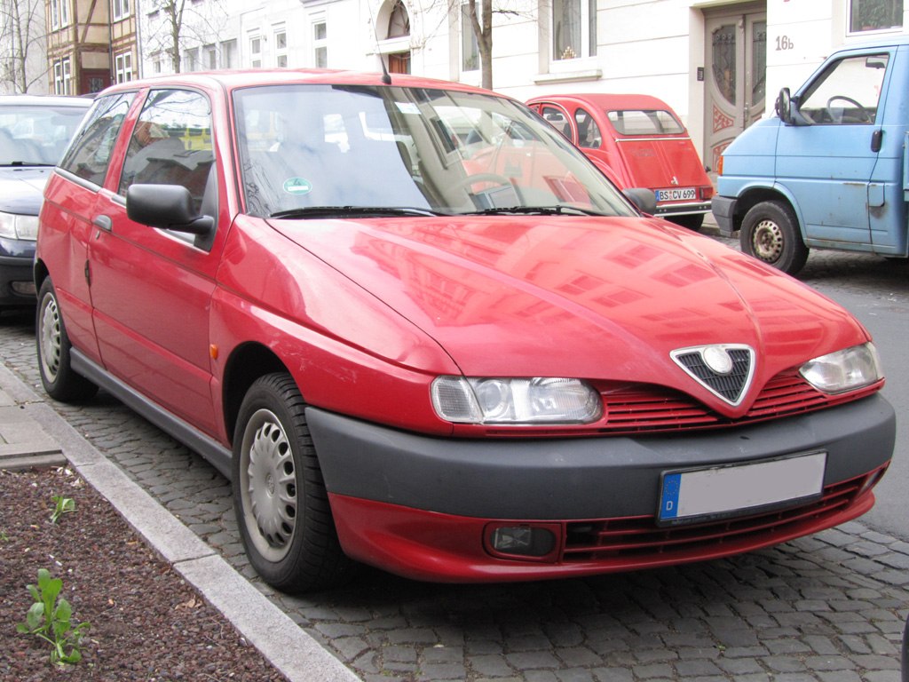 Front side view of red hatchback with unique triangular grille and dual headlights.