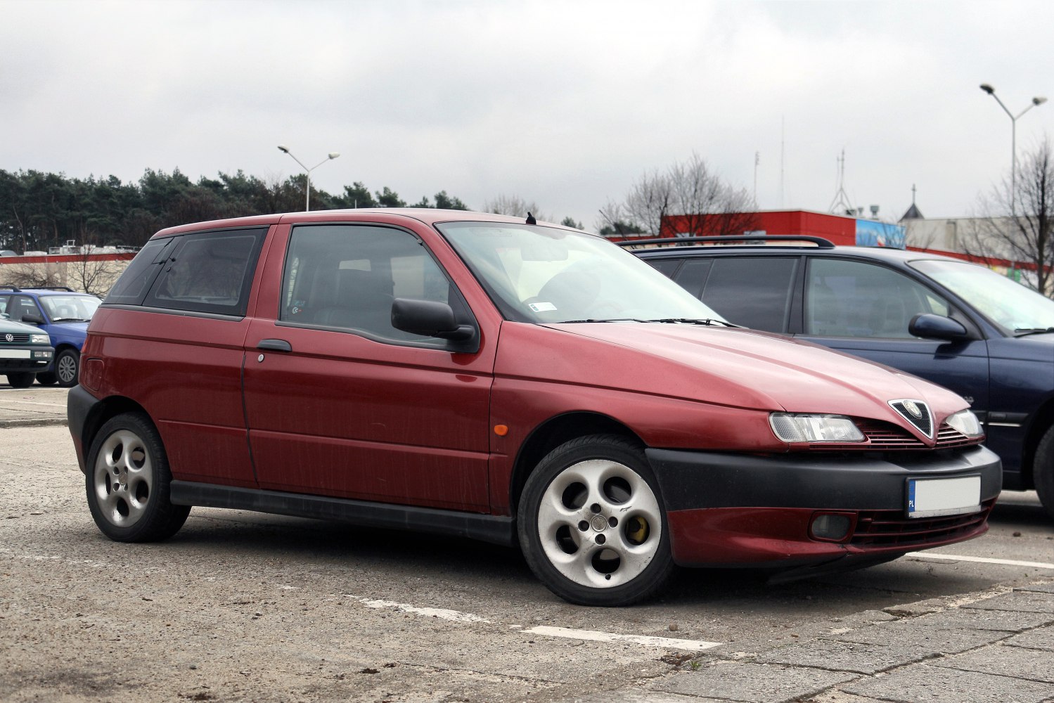 Red hatchback with front side view and round hubcap wheels