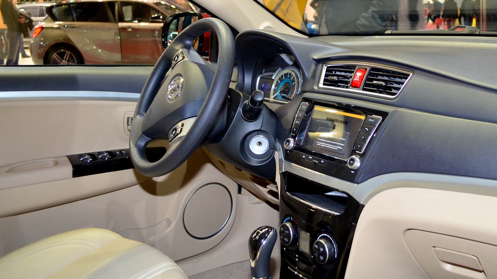 Car interior with steering wheel, dashboard, touchscreen, and beige upholstery