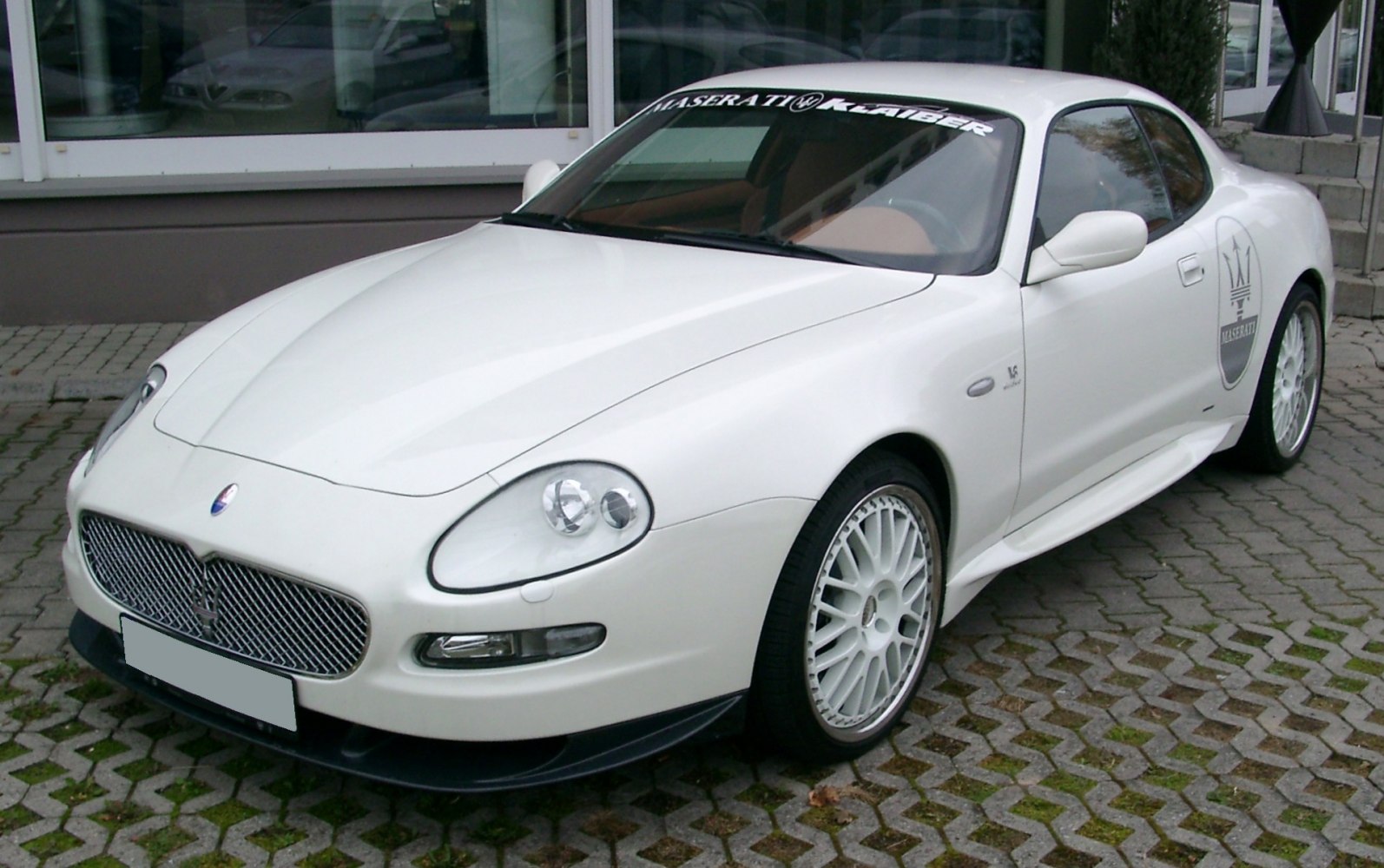Front-side view of a white sporty coupe with mesh grille and multi-spoke wheels