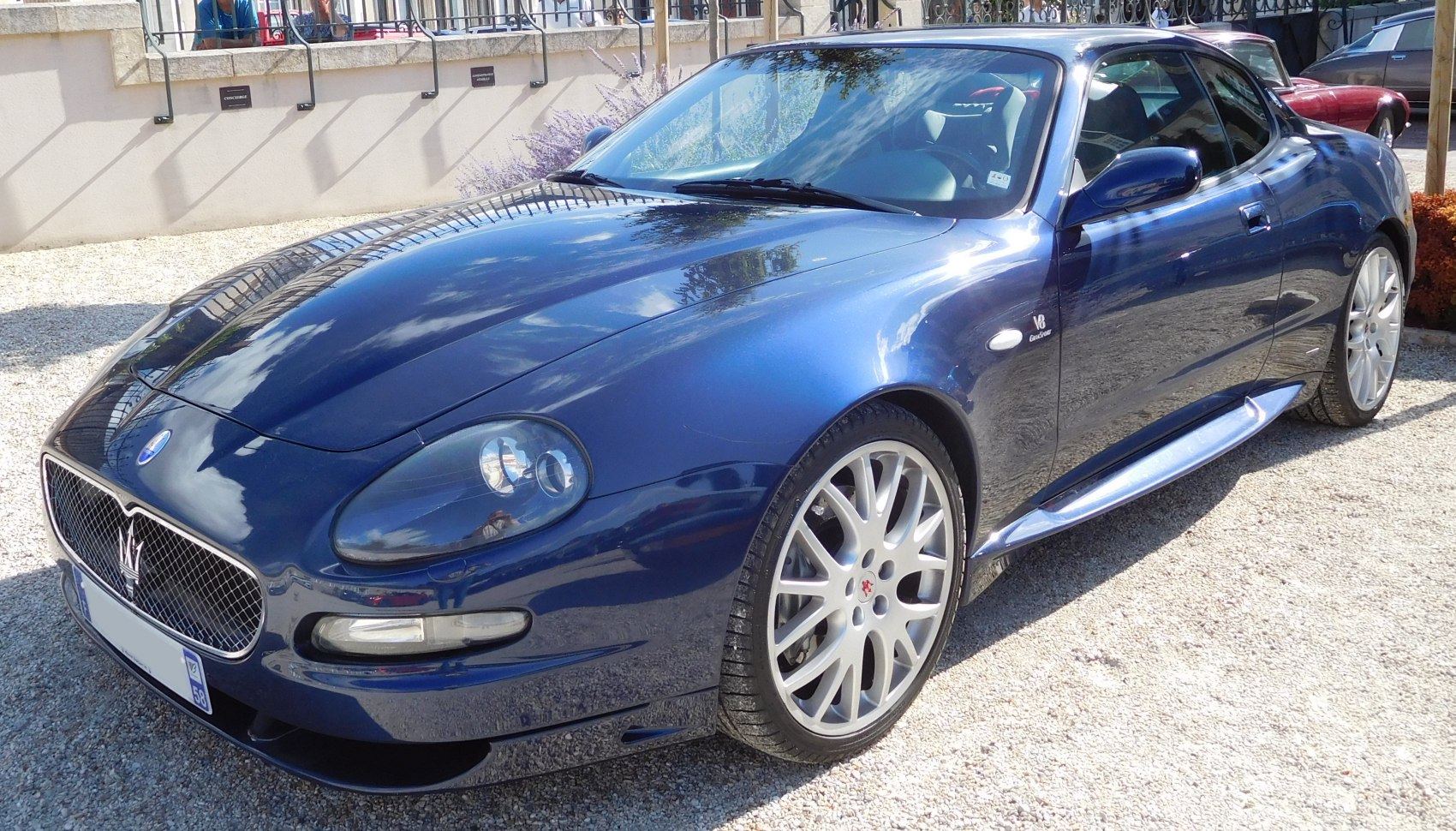 Blue sports coupe front side with V8 badge and alloy wheels