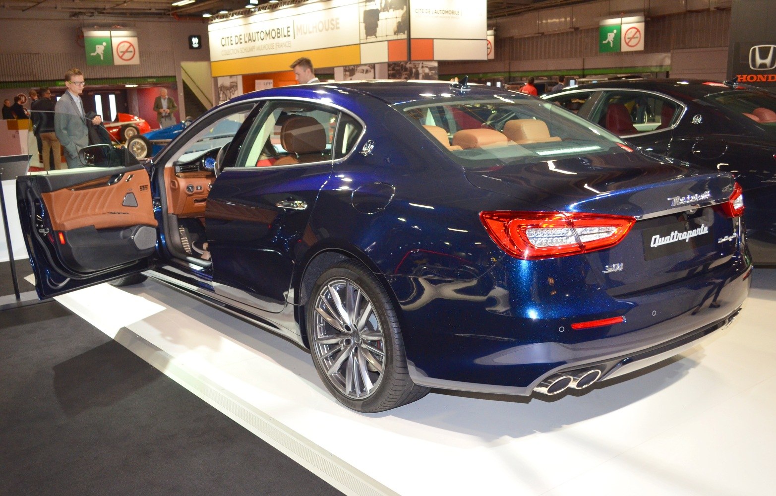 Luxury sedan rear with open door, brown leather interior, dual exhaust.
