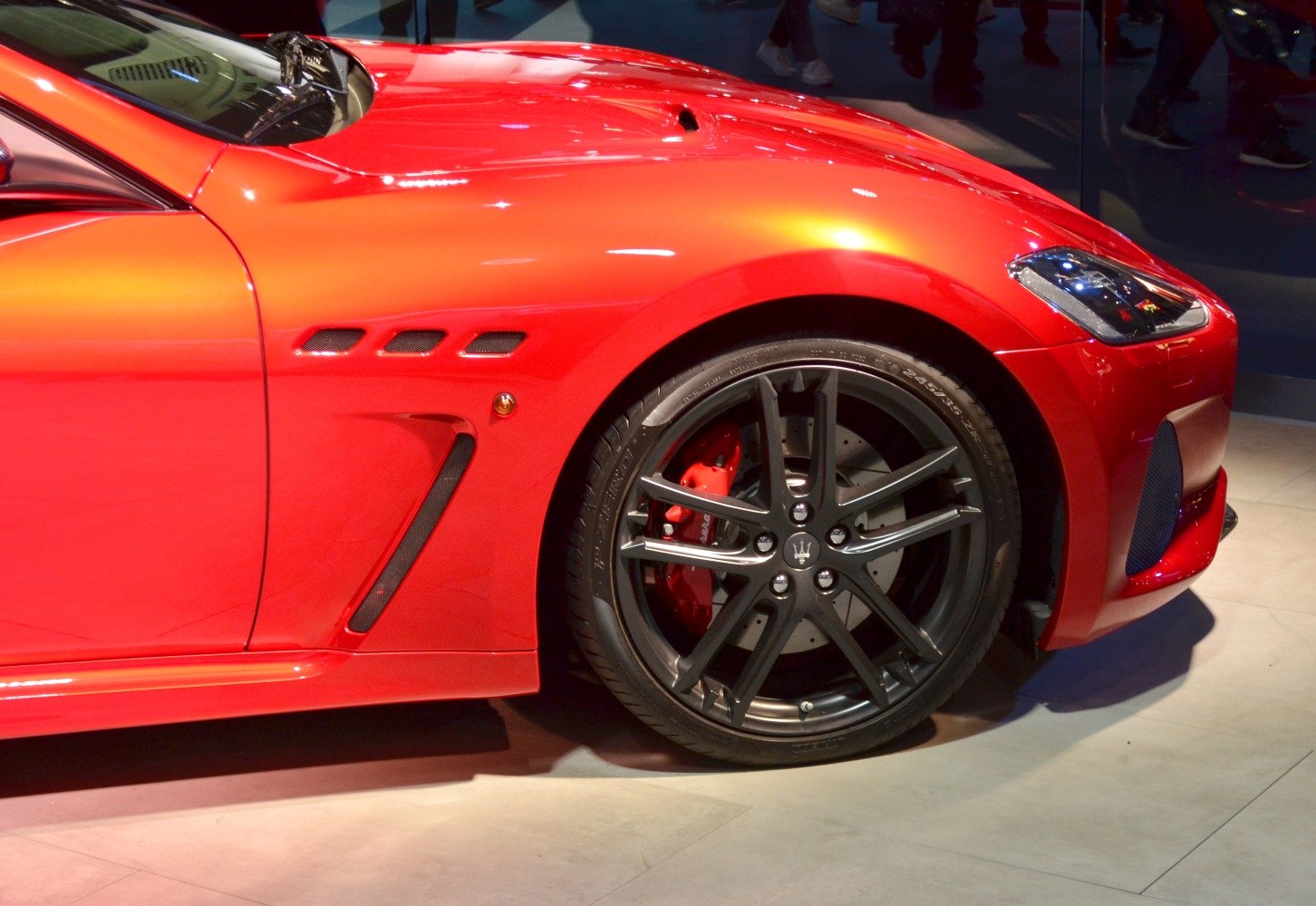 Front wheel with red brake caliper and side air vents on red sports car.