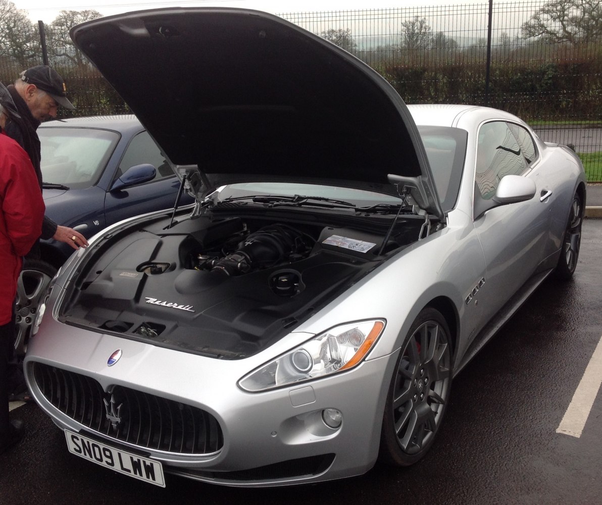 Open hood showing engine bay and front exterior of a luxury coupe
