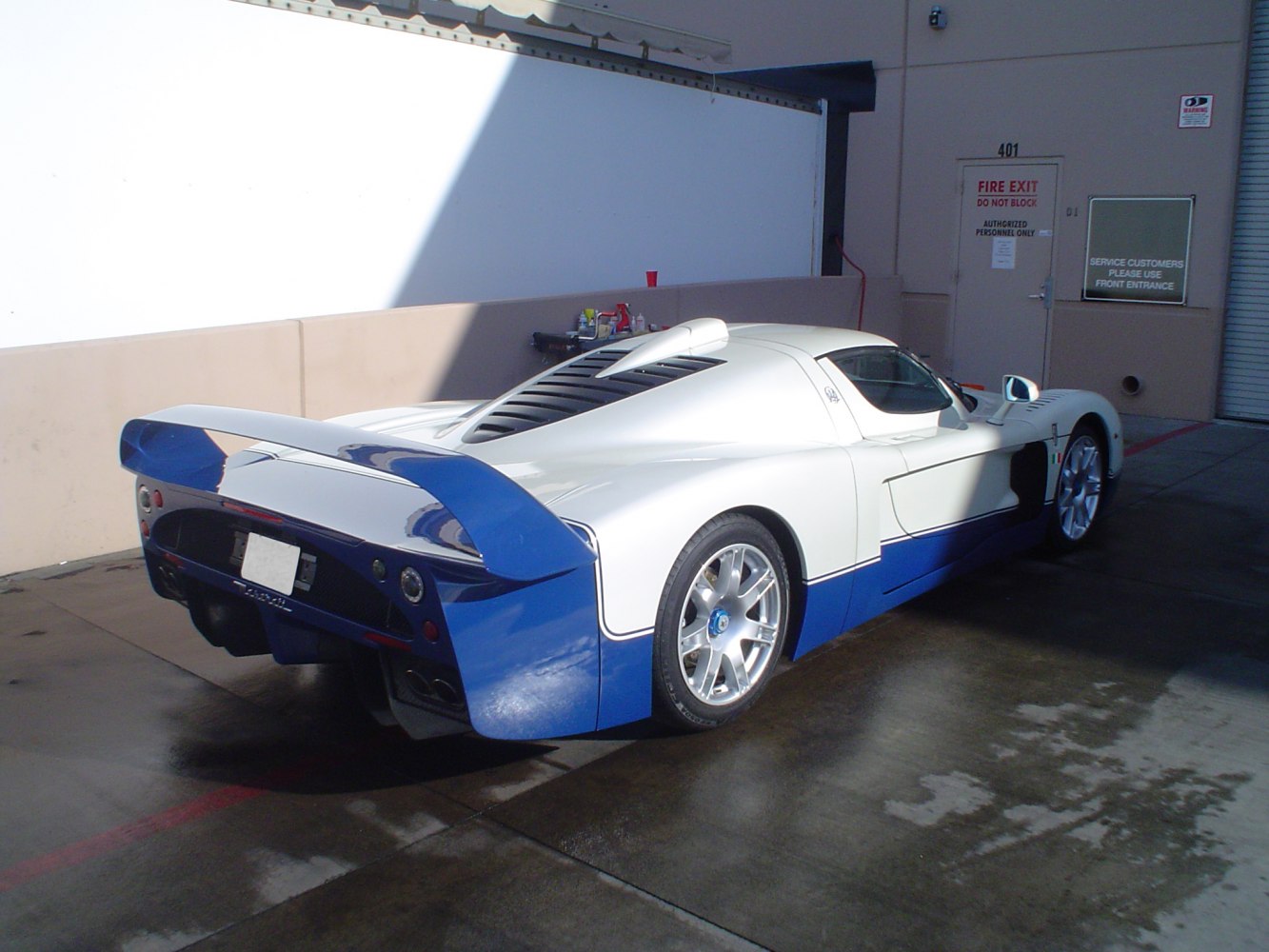 Aerodynamic rear and side of a white and blue supercar with prominent rear wing