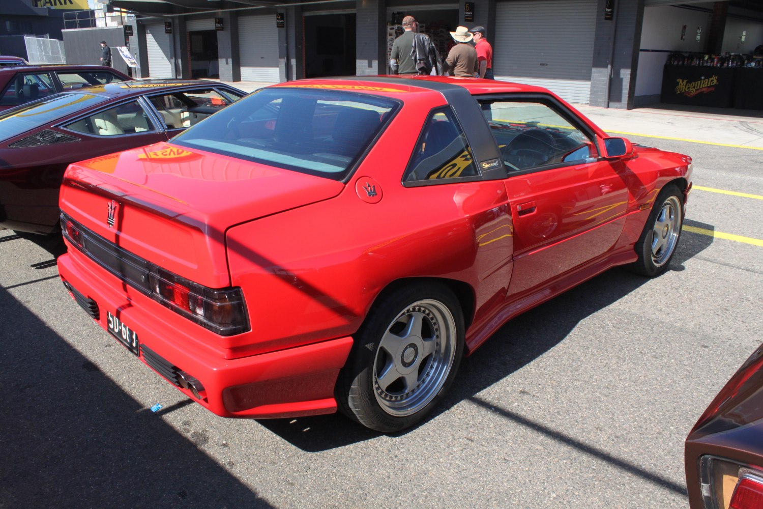 Rear side view of red sports coupe with distinctive alloy wheels and angular design.