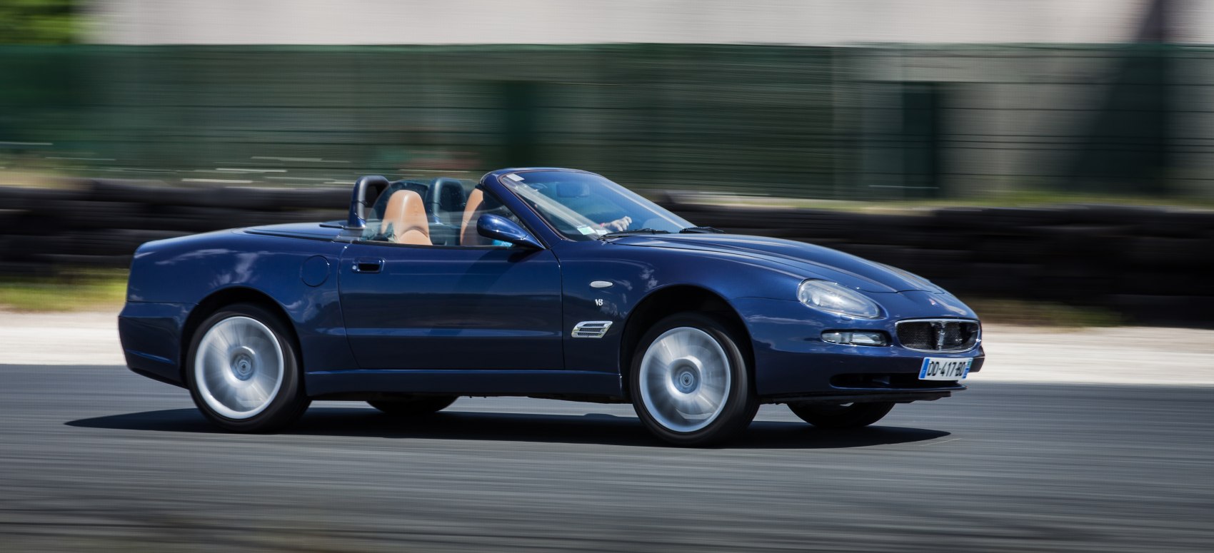 Blue convertible with tan interior moving dynamically on a track