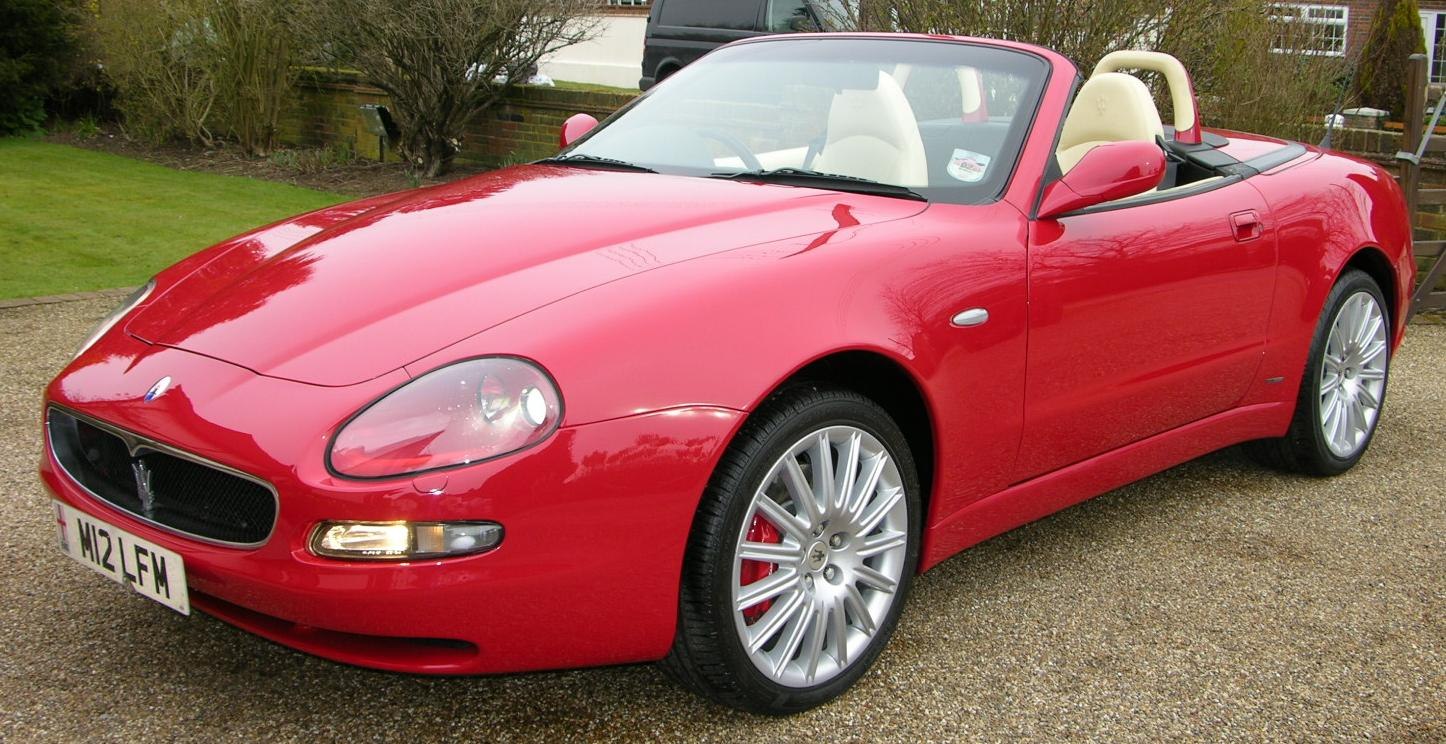 Red convertible sports car front side with alloy wheels and beige interior.
