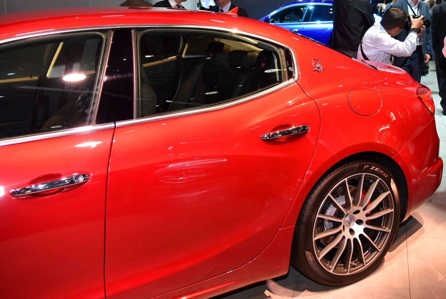 Red car rear side with door, chrome handle, window, and alloy wheel.