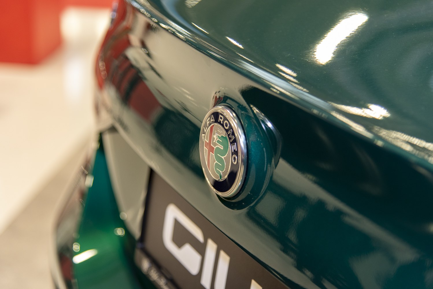 Close-up of a green car's rear badge with an Alfa Romeo emblem.