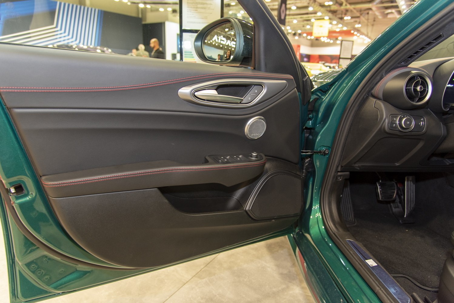 Car interior door panel with black trim and red stitching.