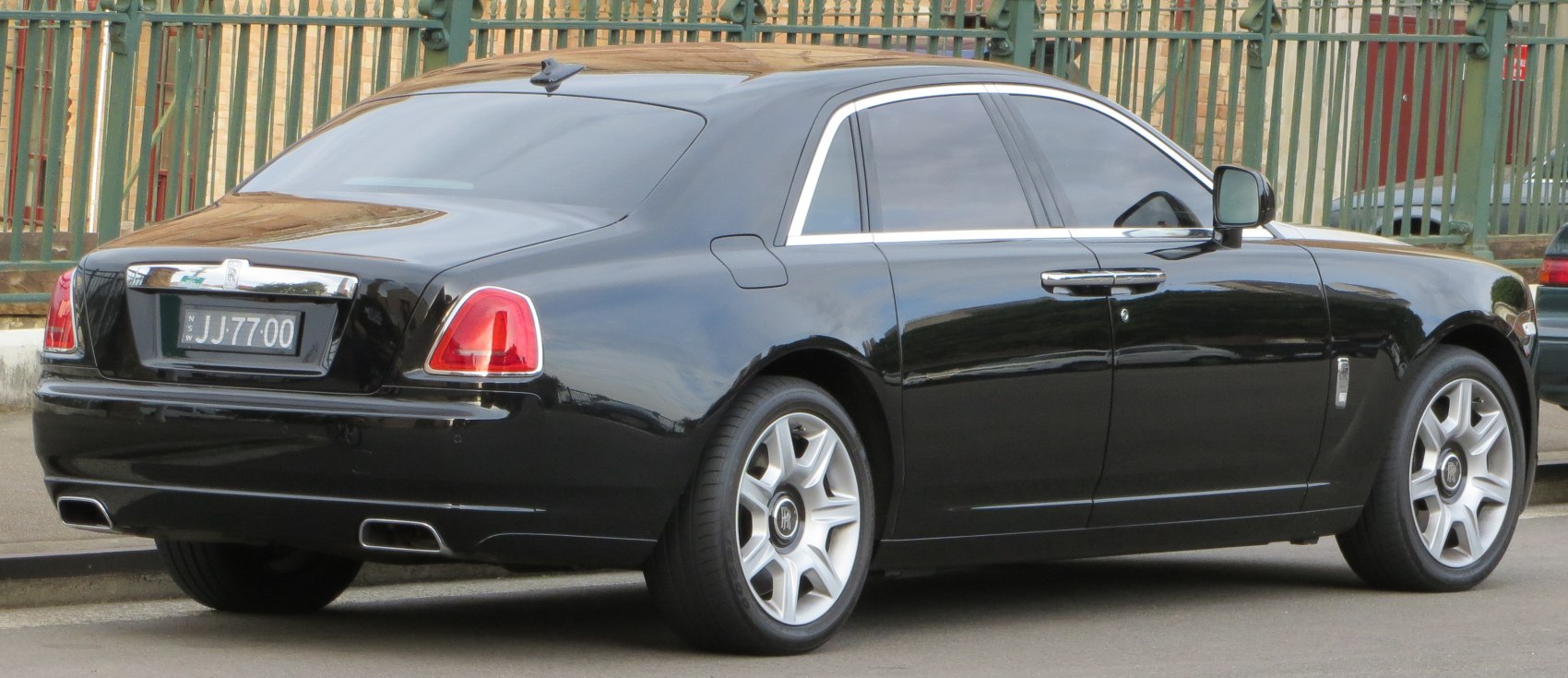 Luxury black sedan rear side profile with tinted windows and dual exhaust.