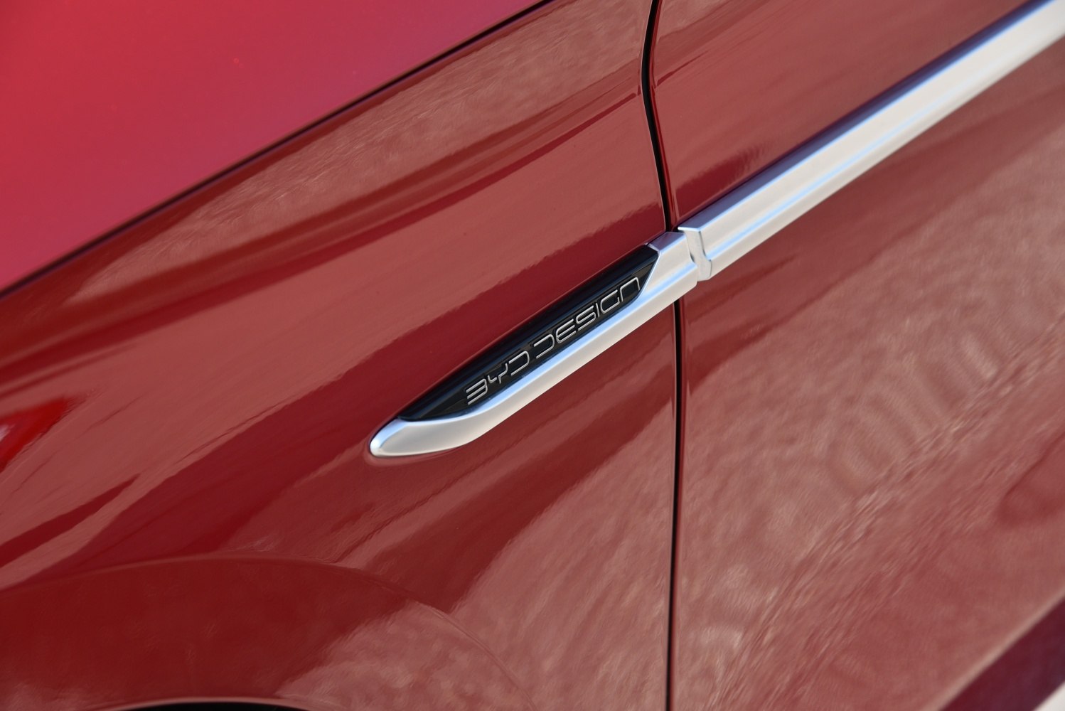 Close-up of sleek side trim with BYD Design emblem on red car surface