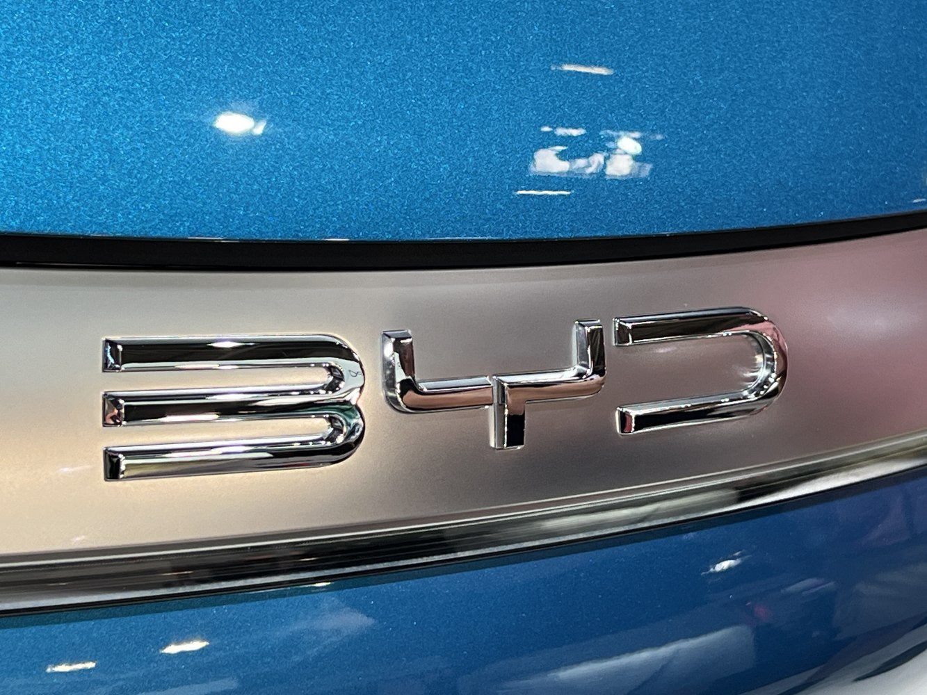 Close-up of chrome BYD emblem badge on blue car surface.