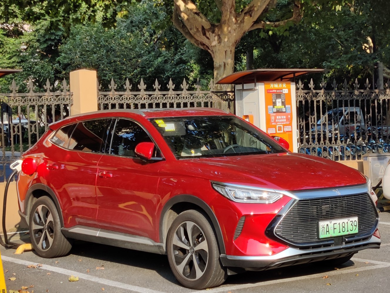 Red electric SUV charging, sleek front grille, urban environment