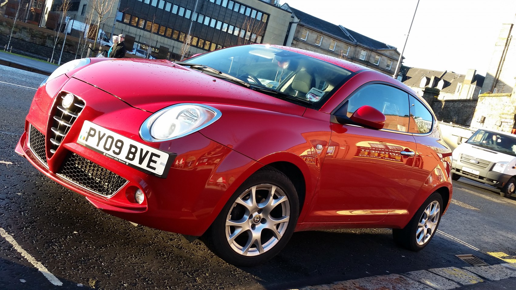 Front side view of red compact hatchback with distinctive grille and alloy wheels