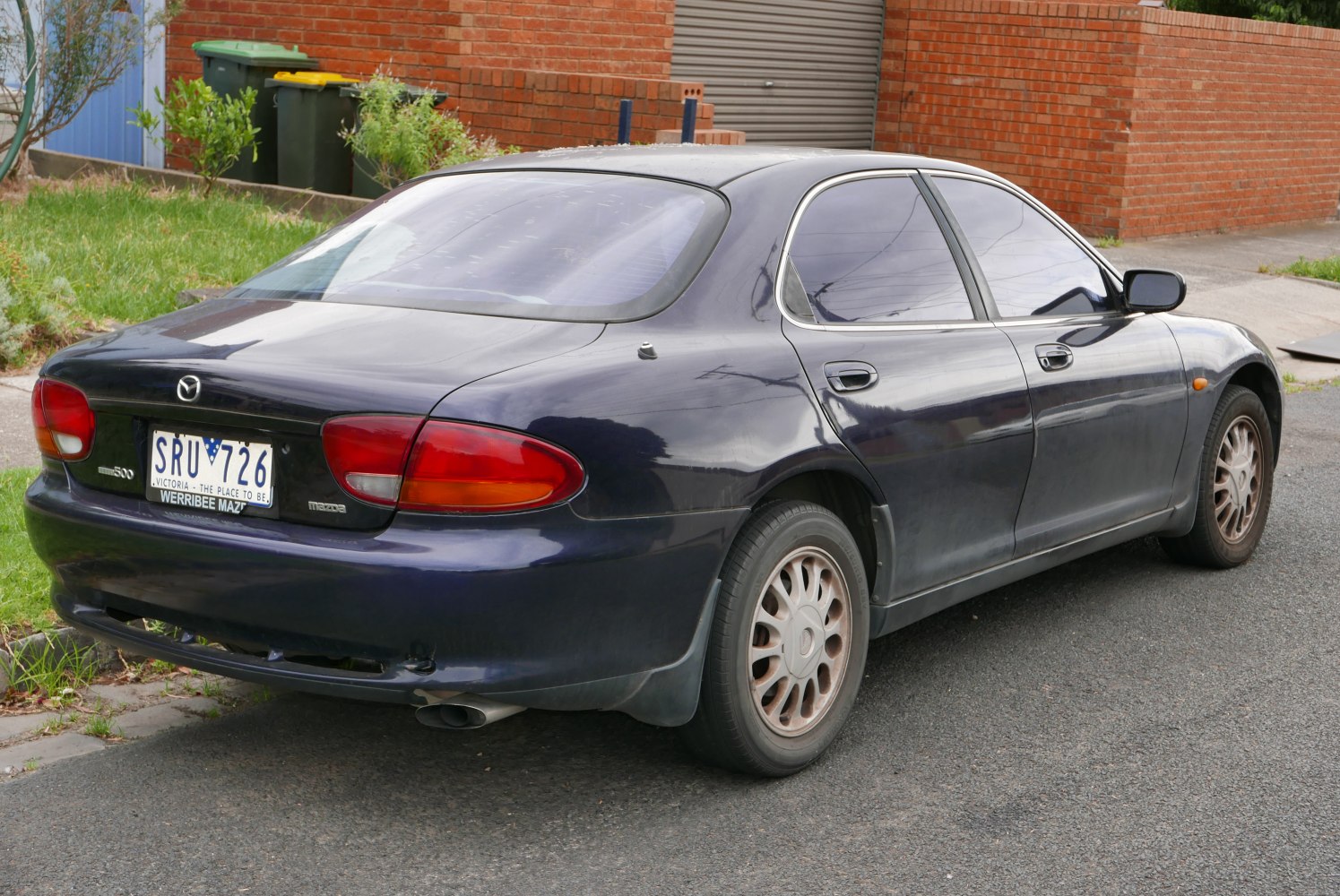Rear side view of a dark blue four-door sedan with distinct taillights and alloy wheels.